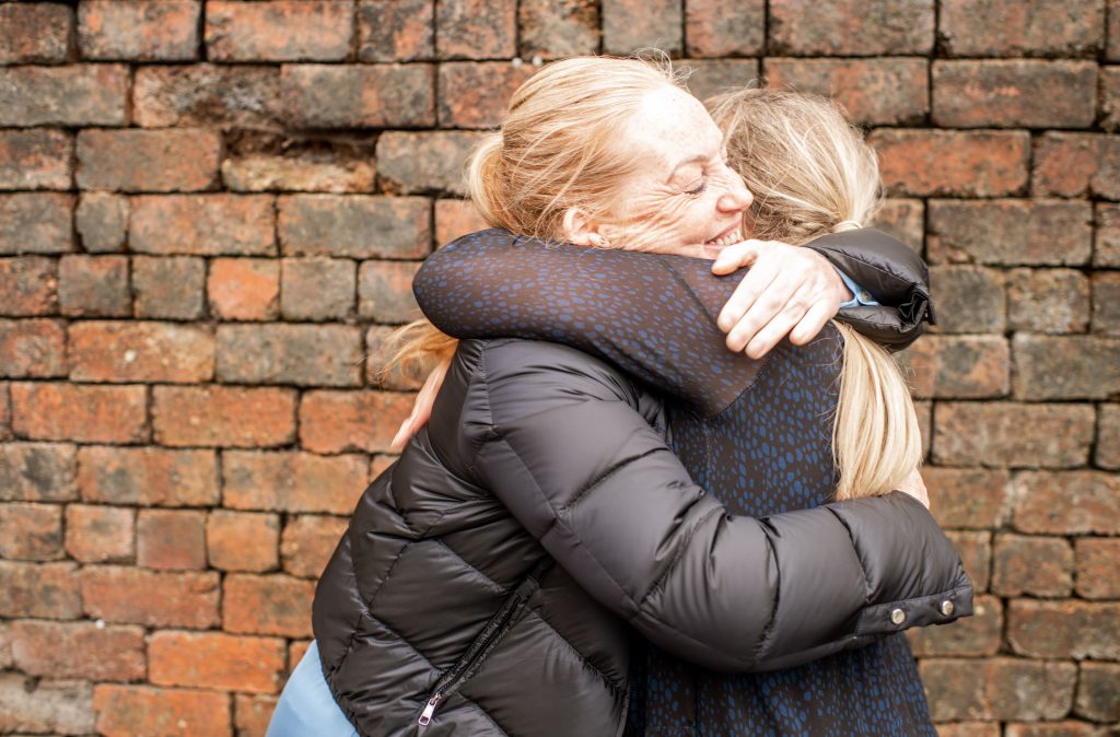 two women hugging in front of a brick wall