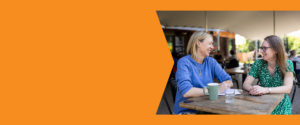 Two ladies sat at a table in a coffee shop chatting and smiling.