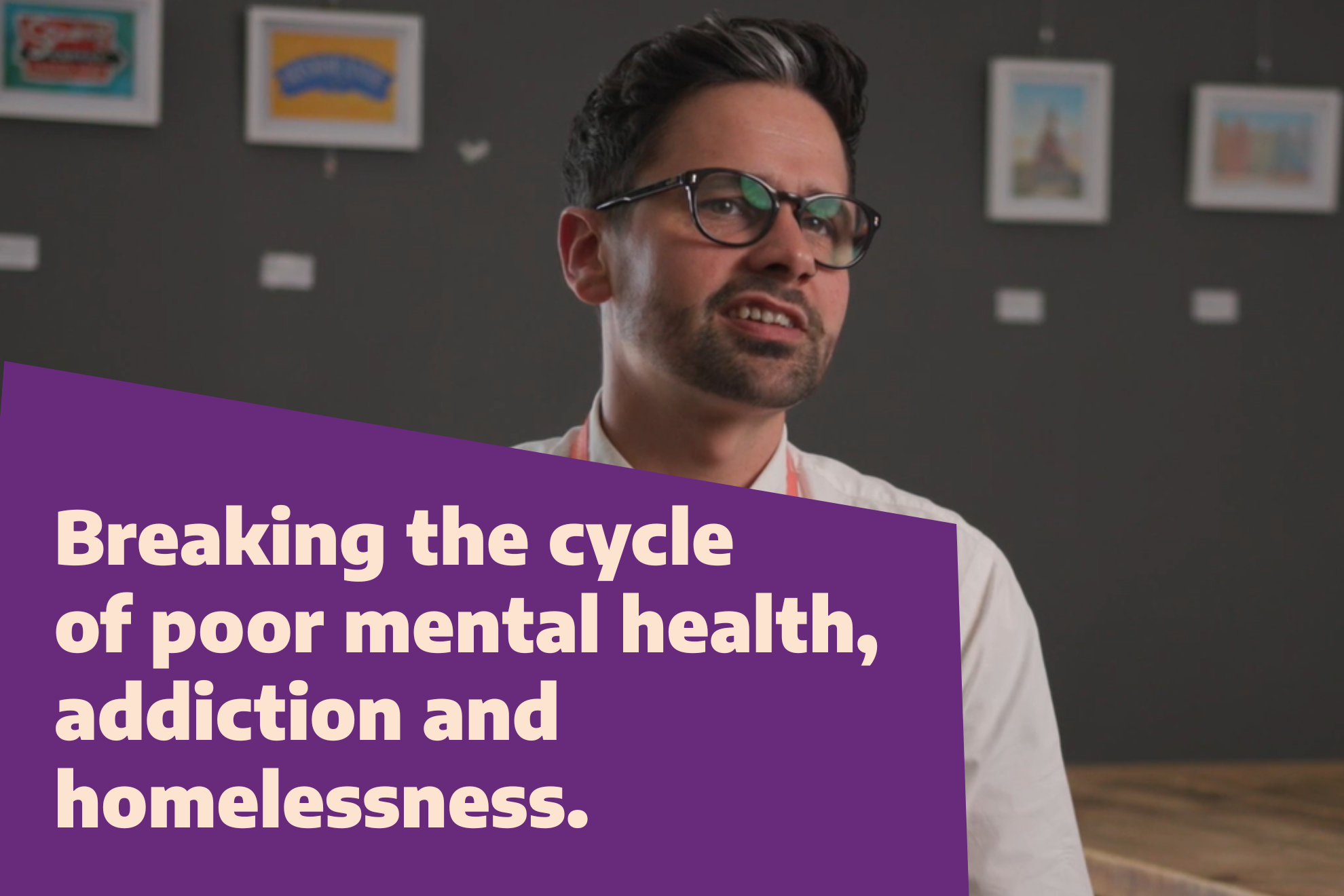 A person with glasses is speaking in front of a dark background with framed pictures. There is a purple overlay on the left side of the image with cream text that reads, 'Breaking the cycle of poor mental health, addiction and homelessness."