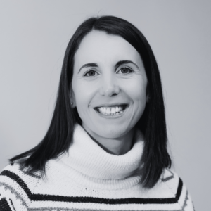 Black-and-white headshot of a person with shoulder-length dark hair, wearing a striped roll-neck jumper and looking at the camera.