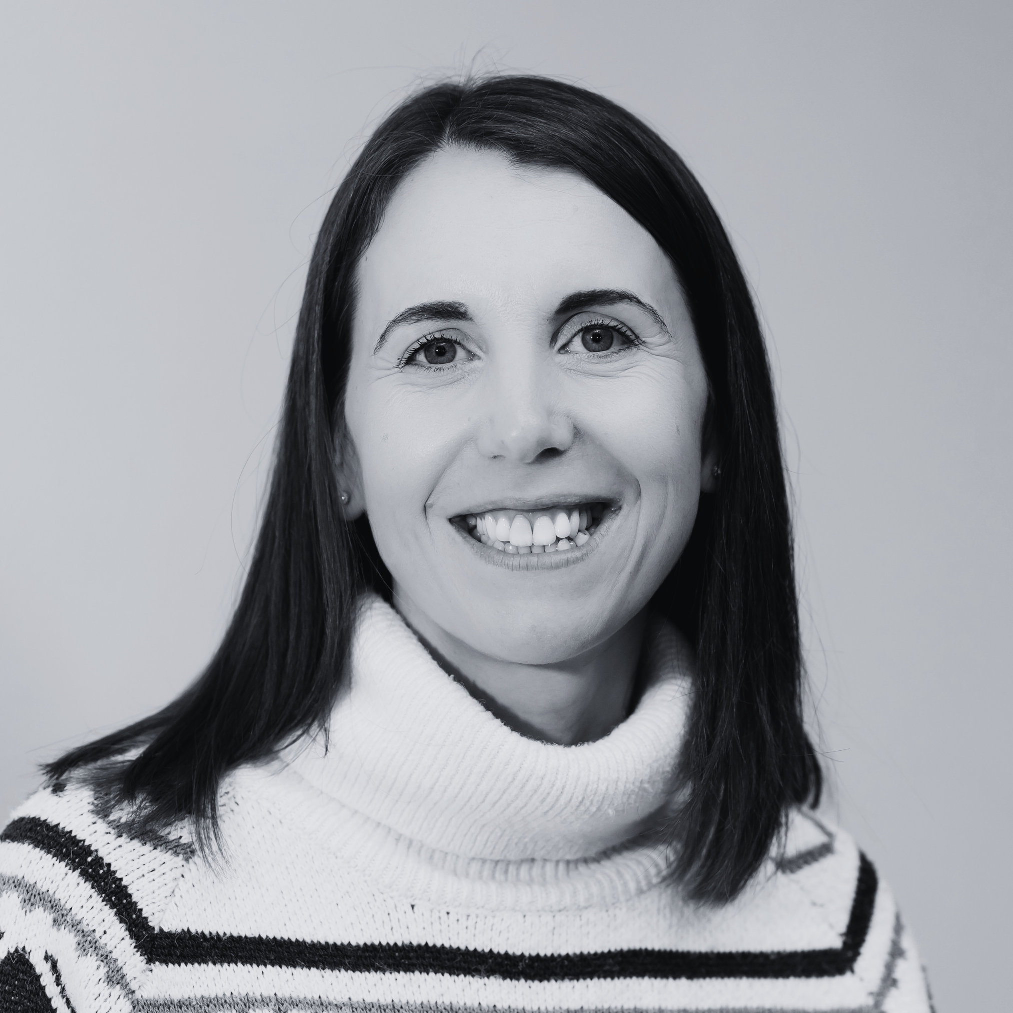 Black-and-white headshot of a person with shoulder-length dark hair, wearing a striped roll-neck jumper and looking at the camera.