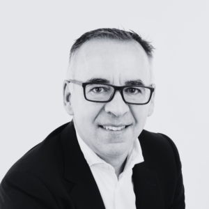 Black-and-white headshot of a person wearing glasses, a dark jacket and white shirt, against a plain light background.
