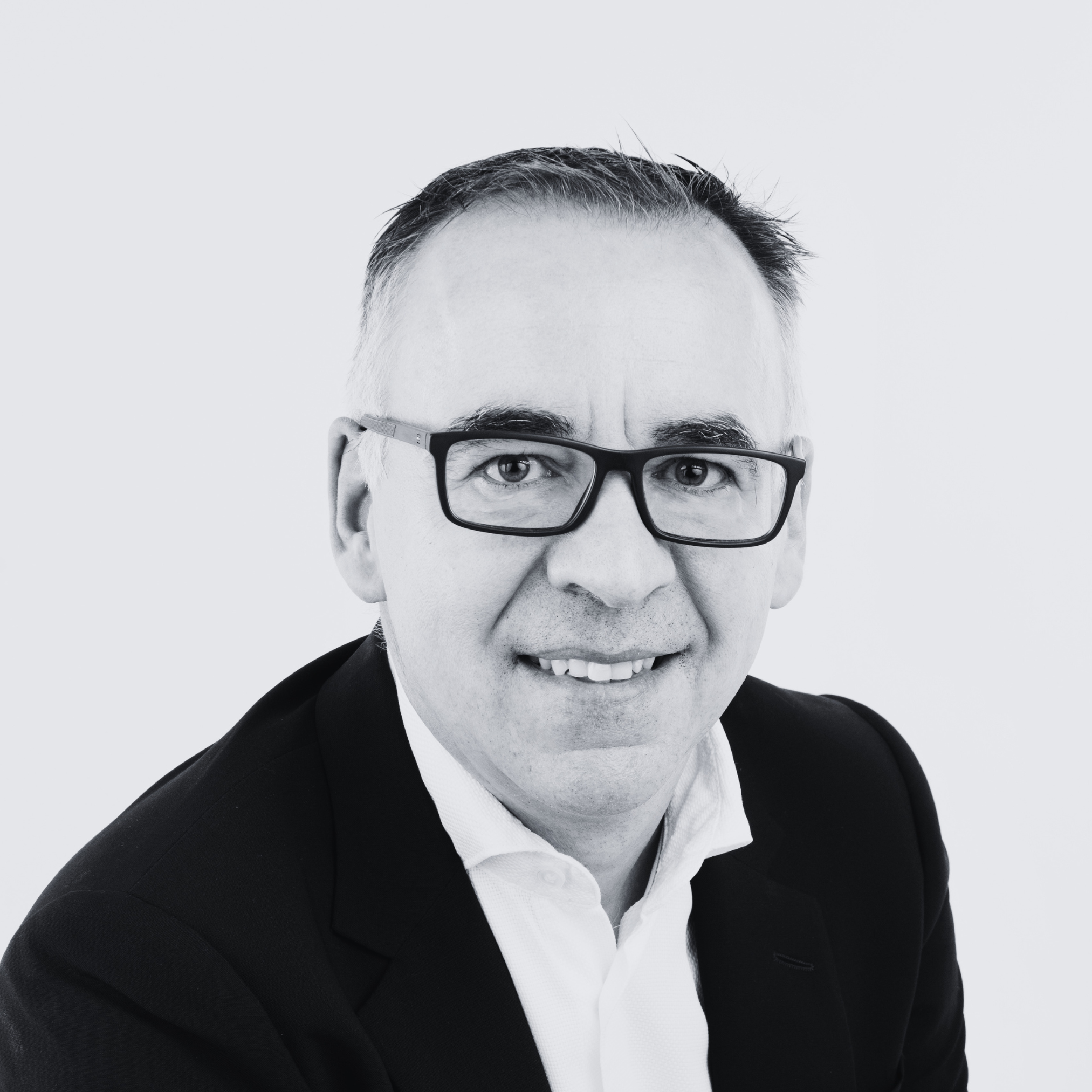 Black-and-white headshot of a person wearing glasses, a dark jacket and white shirt, against a plain light background.