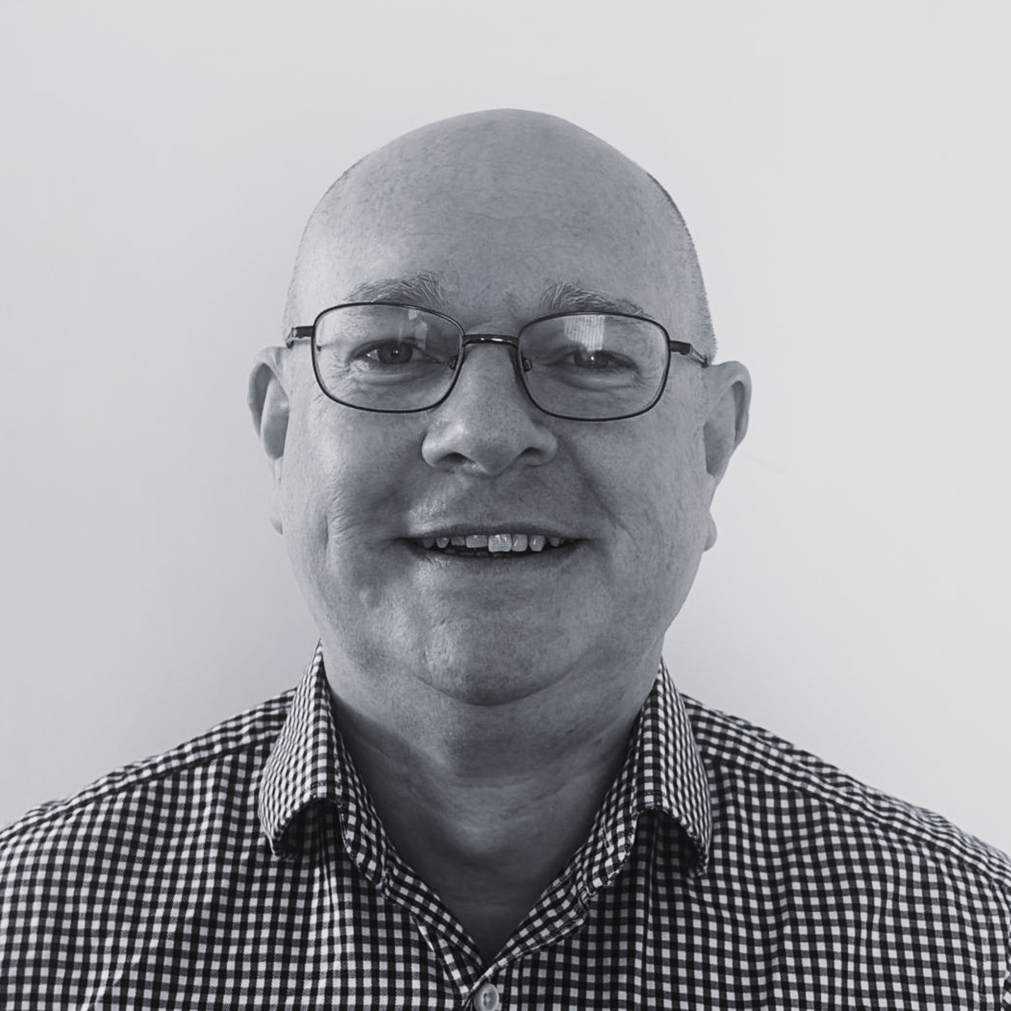 Black-and-white head-and-shoulders portrait of a person wearing glasses and a checked shirt, facing the camera against a plain background.